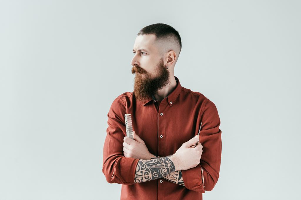 barbero guapo barbudo sosteniendo peine y tijeras en brazos cruzados aislados en blanco
 - Foto, imagen