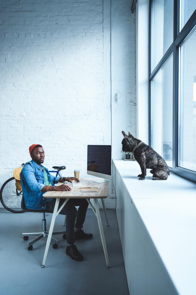 Csinos afroamerikai férfi dolgozó francia bulldog ablakpárkányon ül míg számítógép - Fotó, kép