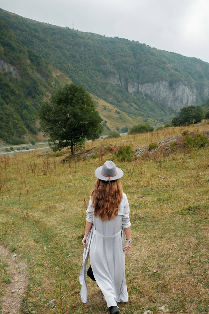 Tyttö hatussa kävelee lähellä vuoria.
 - Valokuva, kuva