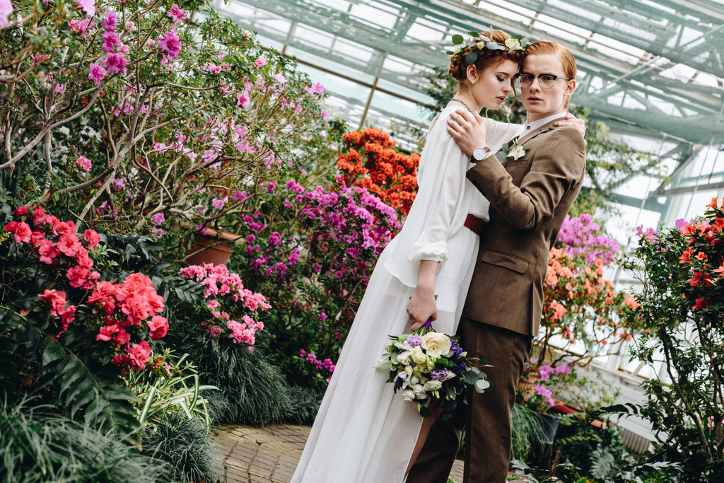 schönes zartes junges Hochzeitspaar mit Blumenstrauß im botanischen Garten - Foto, Bild