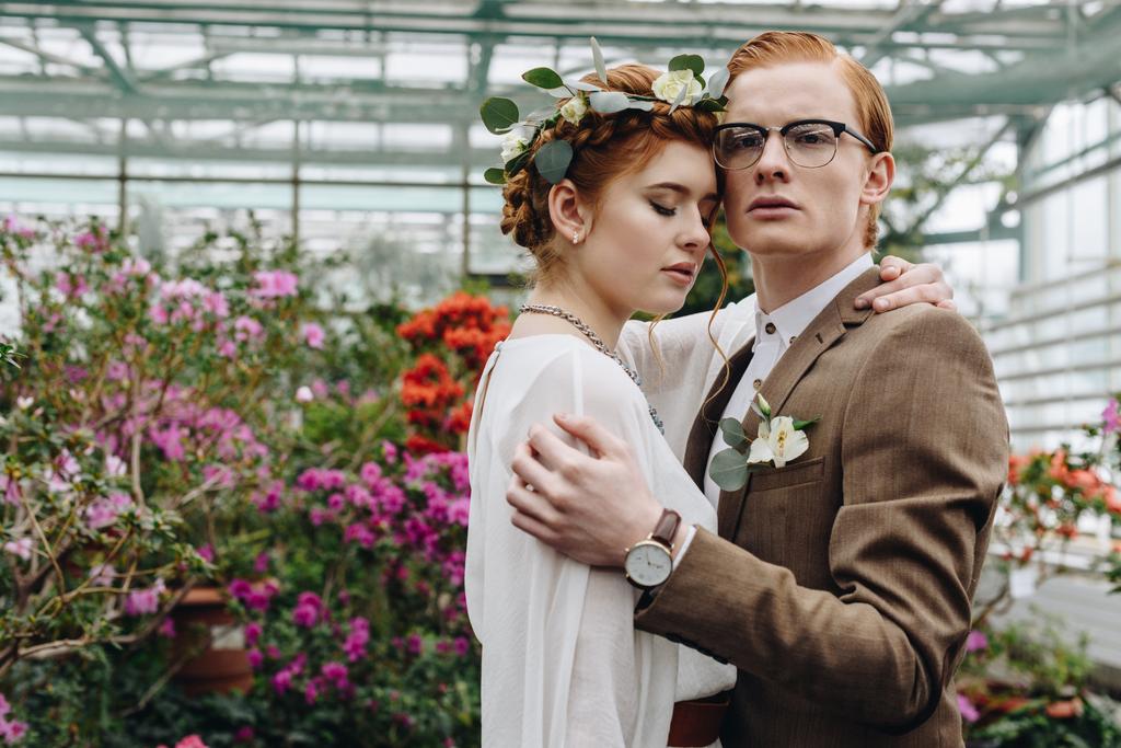 řízení, mladý zrzavý svatební pár všeobjímající stoje mezi květy v botanické zahradě - Fotografie, Obrázek