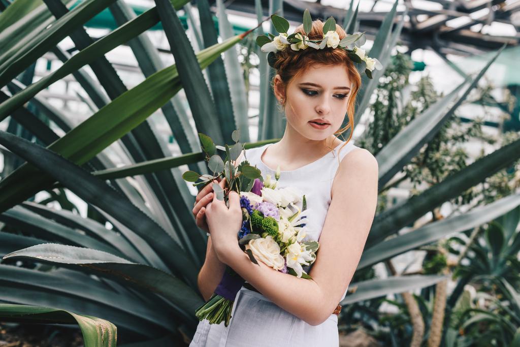 beautiful tender young redhead bride holding wedding bouquet in botanical garden  - Photo, Image