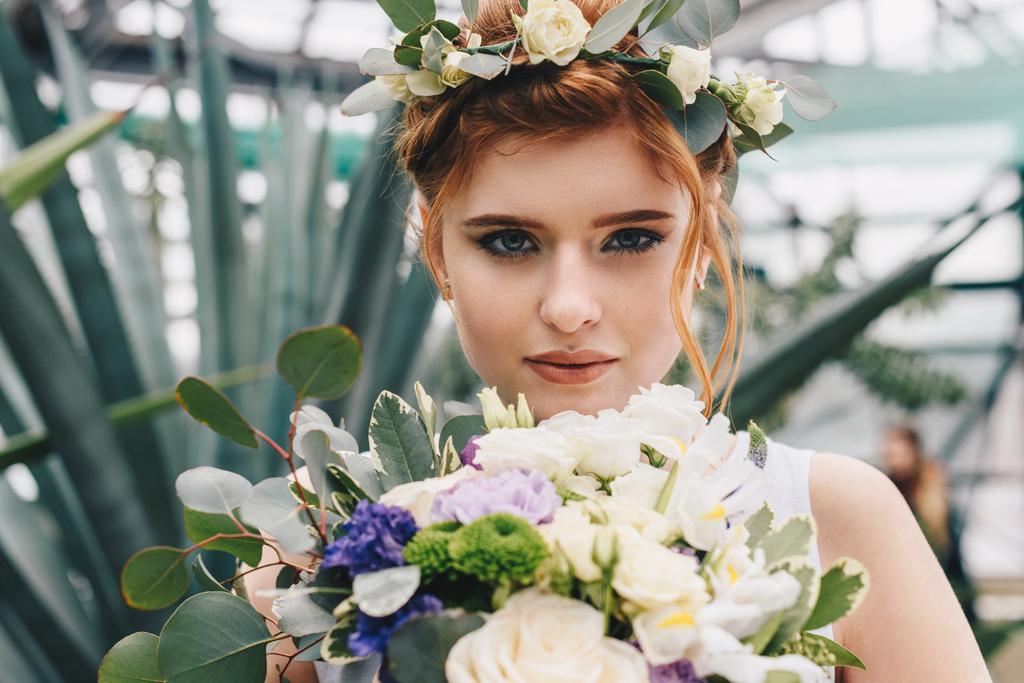 gyönyörű fiatal menyasszony, virág koszorú, esküvői csokor gazdaság és látszó-on fényképezőgép  - Fotó, kép