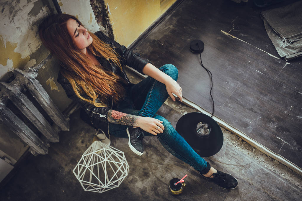 retrato de mujer de moda joven con pelo rojo y tatuaje en ropa negra sentado en el suelo en la habitación de estilo vintage
.  - Foto, imagen