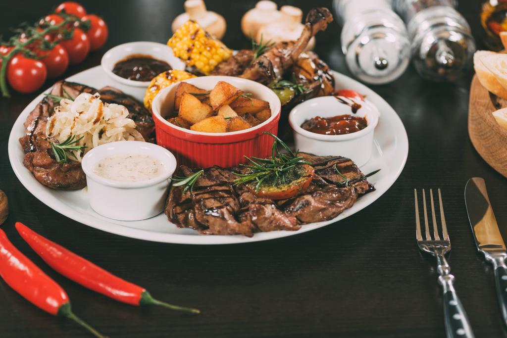 тарілка з соусами, смажена картопля, смажене м'ясо та овочі на столі
  - Фото, зображення