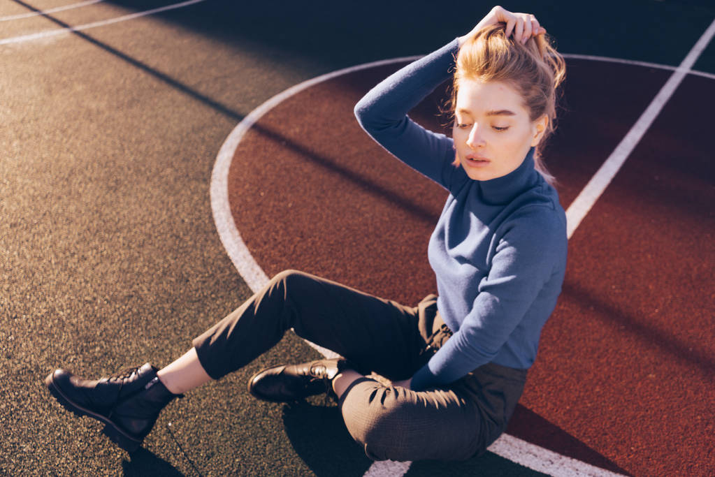 Stylový důvěru mladé blond modelka dívka sedí na hřišti na podlaze, v paprscích slunce na jaře - Fotografie, Obrázek