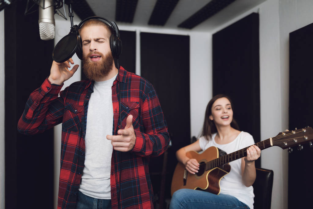 Un homme et une femme chantent une chanson dans un studio d'enregistrement. Un homme chante, et une femme joue de la guitare
. - Photo, image
