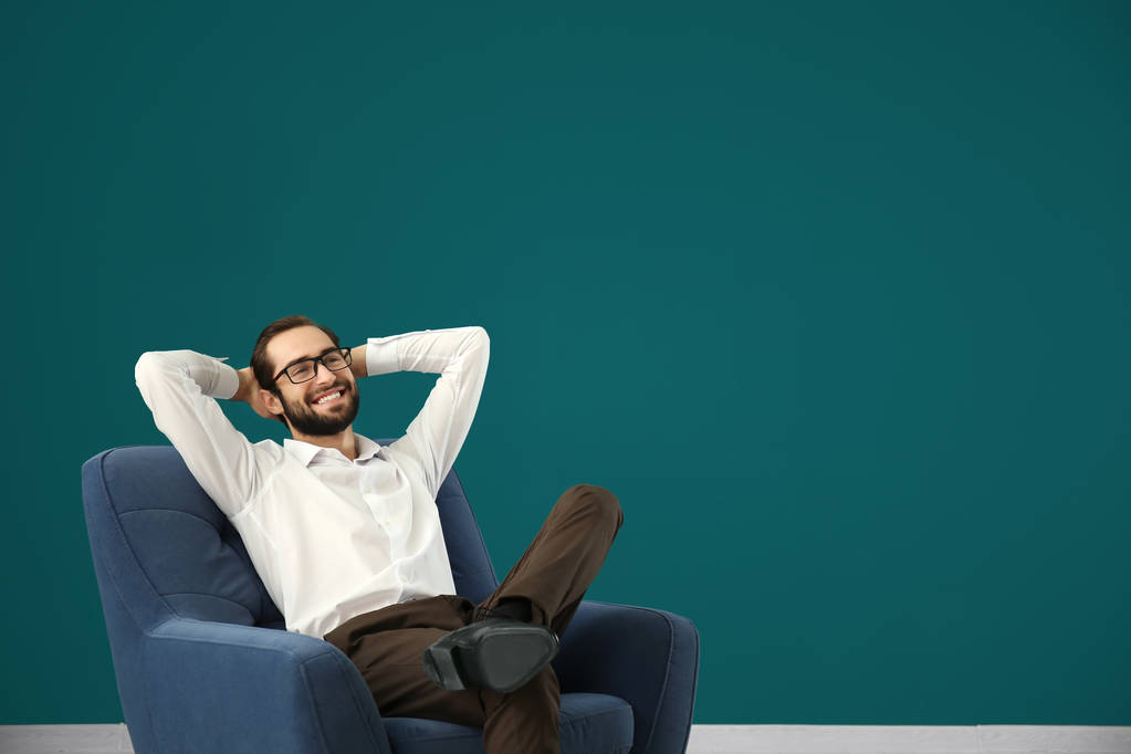 Hombre guapo relajándose en cómodo sillón contra la pared de color
 - Foto, Imagen