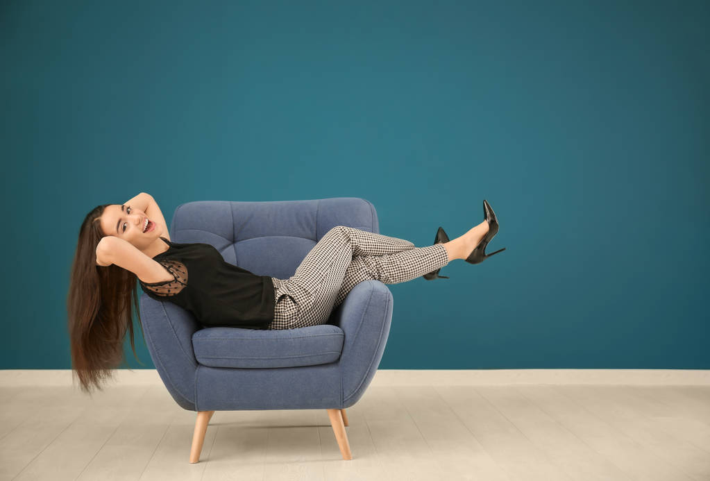 schöne junge Frau entspannt sich in bequemen Sessel gegen Farbwand - Foto, Bild