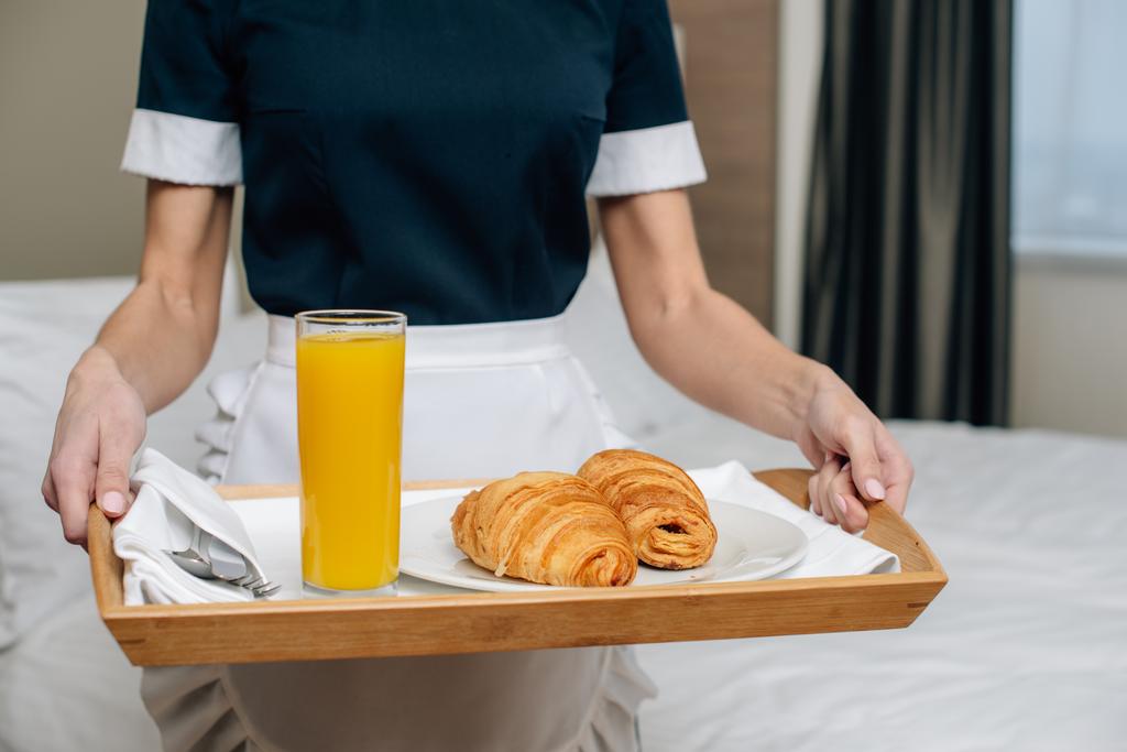 Schnappschuss von Dienstmädchen in Uniform mit Croissants und Saft auf Tablett in Hotelsuite - Foto, Bild