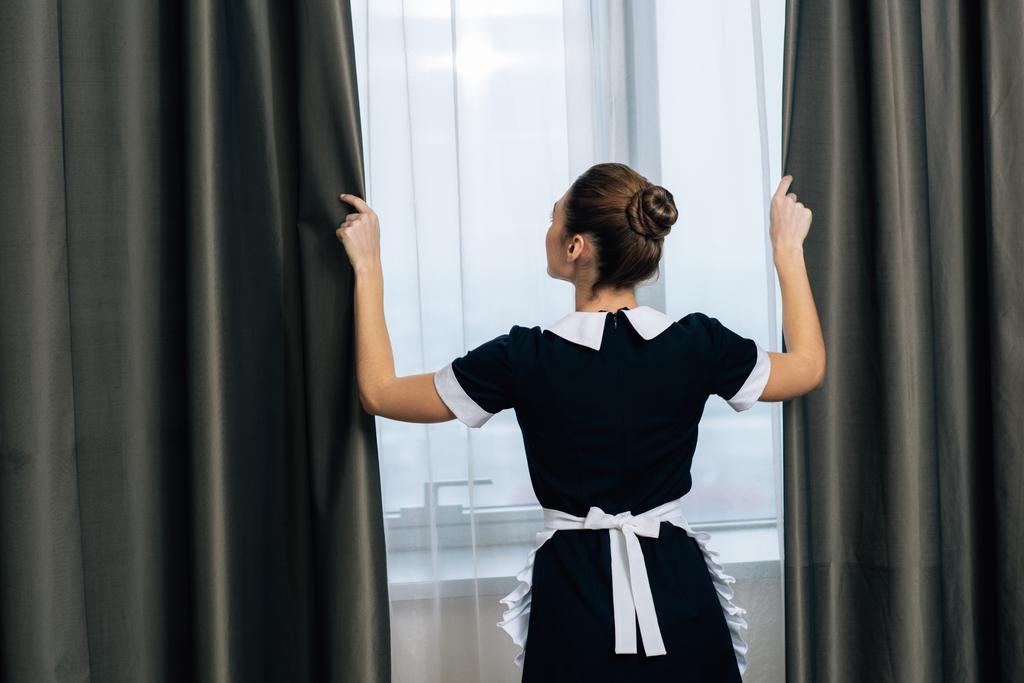 vue arrière de jeune belle femme de ménage en uniforme rideaux de fermeture
 - Photo, image