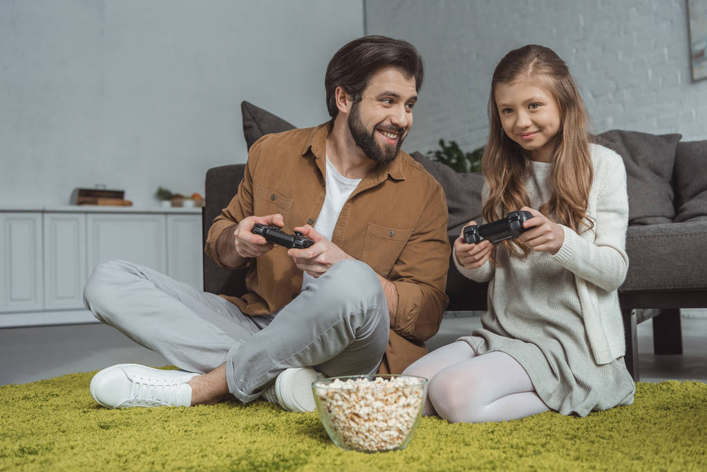 apa és lánya, ül a szőnyegen, és a videó lejátszás game - Fotó, kép