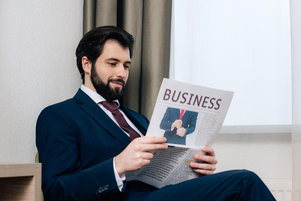 glimlachend knappe zakenman lezing krant in hotelkamer - Foto, afbeelding