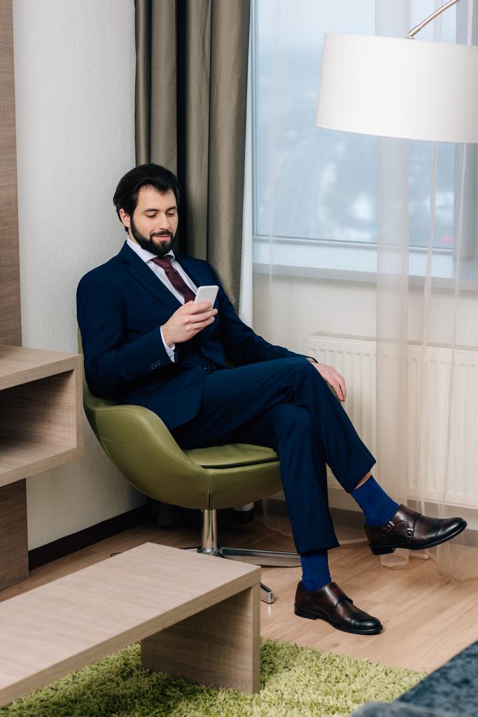 uomo d'affari sorridente utilizzando smartphone mentre seduto in poltrona
 - Foto, immagini