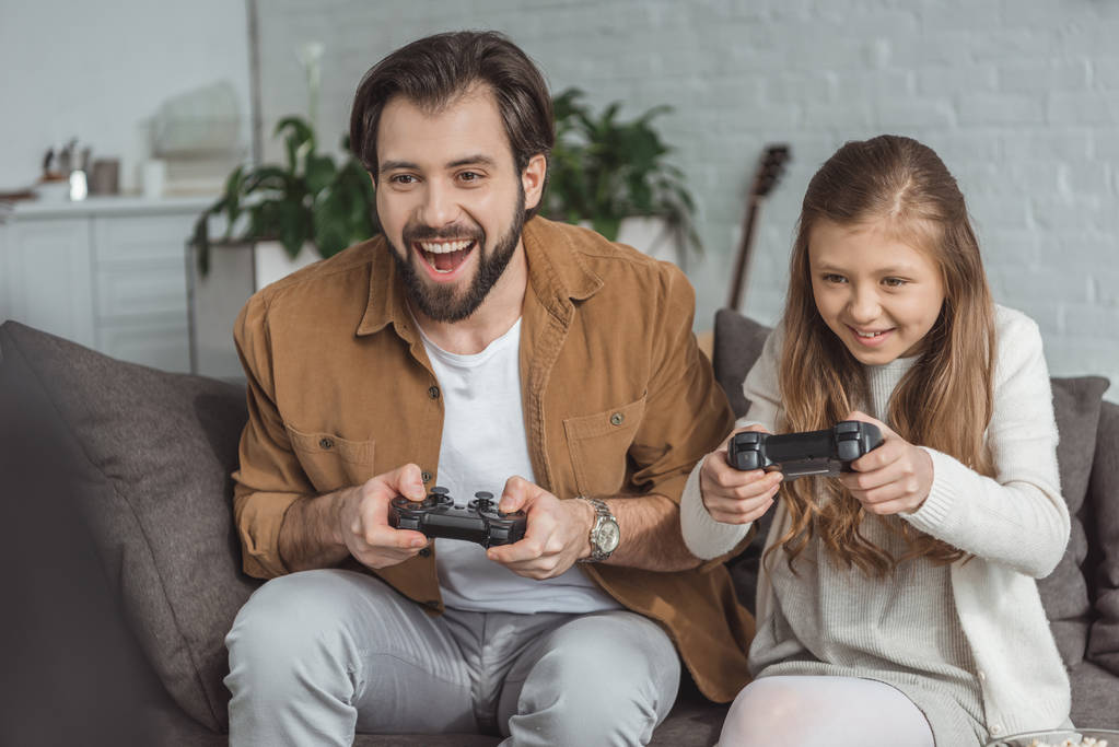 Feliz padre e hija jugando videojuegos en casa
 - Foto, Imagen