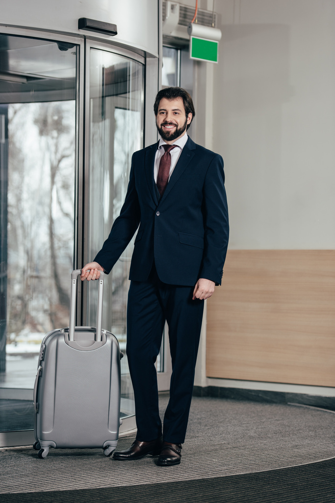 homem de negócios bonito sorridente com bagagem saindo do hotel
 - Foto, Imagem