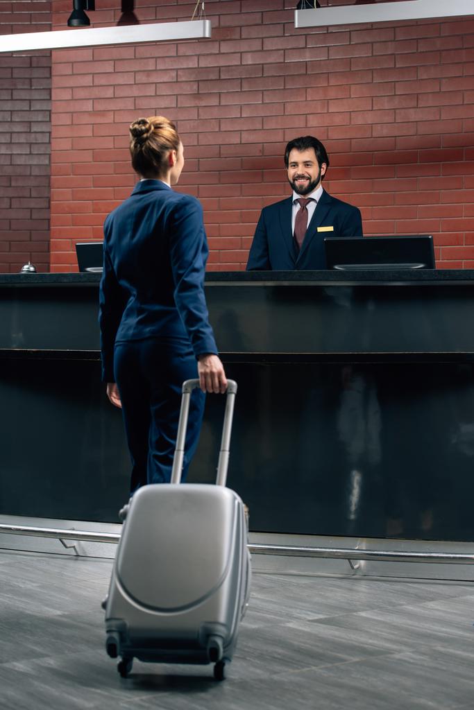 Geschäftsfrau geht mit Gepäck an Hotelrezeption - Foto, Bild