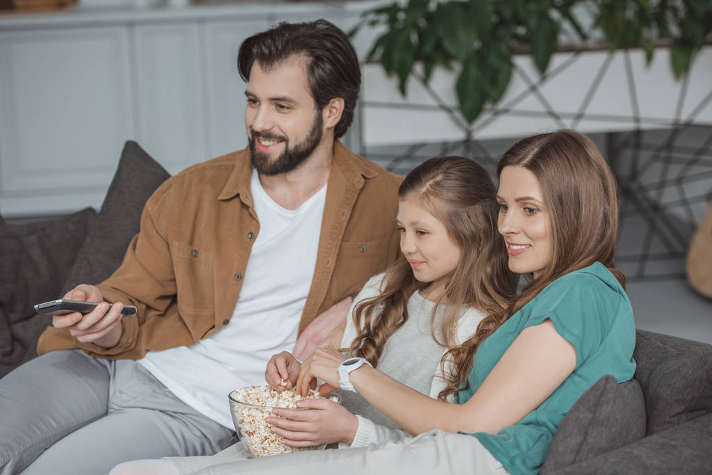 ευτυχείς γονείς και κόρη βλέποντας τηλεόραση με ποπ κορν στο σπίτι - Φωτογραφία, εικόνα