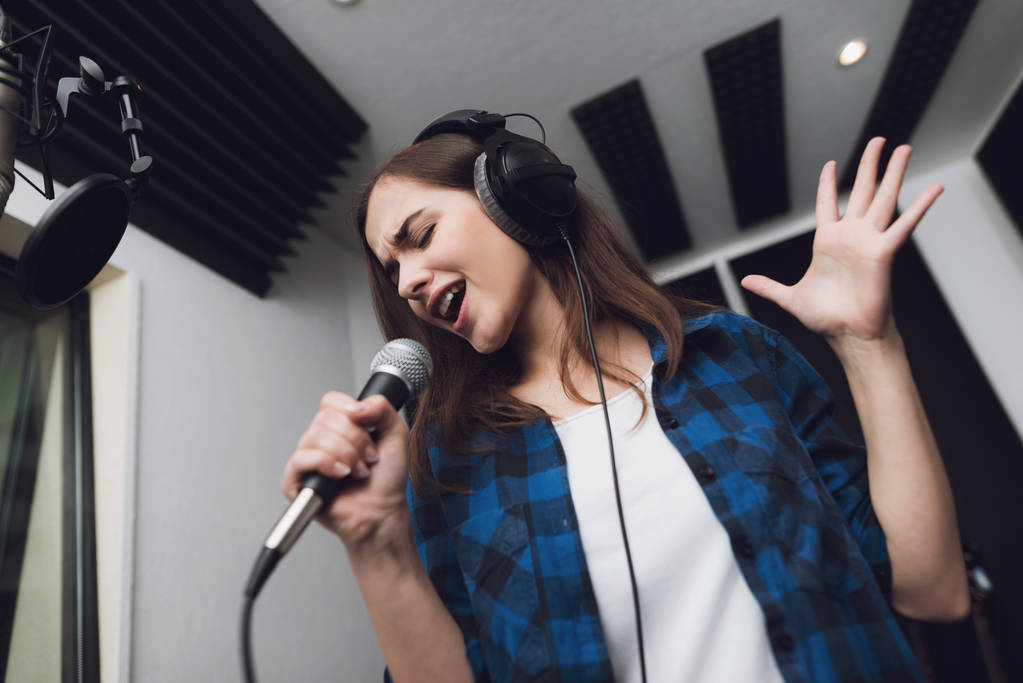 A lány énekel dalt egy modern stúdió. Ő énekel a dal nagyon érzelmileg. Előtte van egy stúdió mikrofon. - Fotó, kép