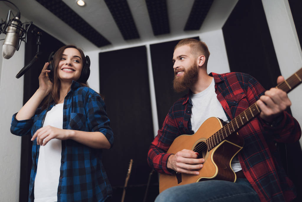 ein Mädchen und ein Mann singen in einem modernen Tonstudio ein Lied zu einer Gitarre. das Mädchen singt, und der Kerl spielt Gitarre. - Foto, Bild