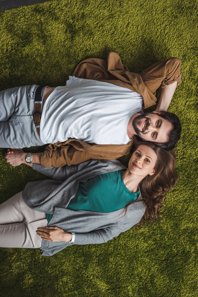 bovenaanzicht van aantrekkelijke paar liggend op het groene tapijt thuis - Foto, afbeelding