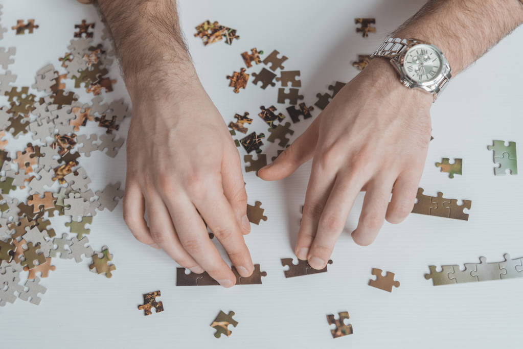 immagine ritagliata di uomo che collega pezzi di puzzle a tavola
 - Foto, immagini