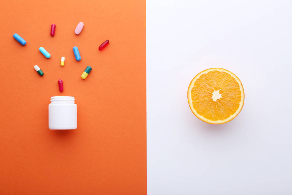 Помаранчеві фрукти і барвисті таблетки в білій пляшці
 - Фото, зображення