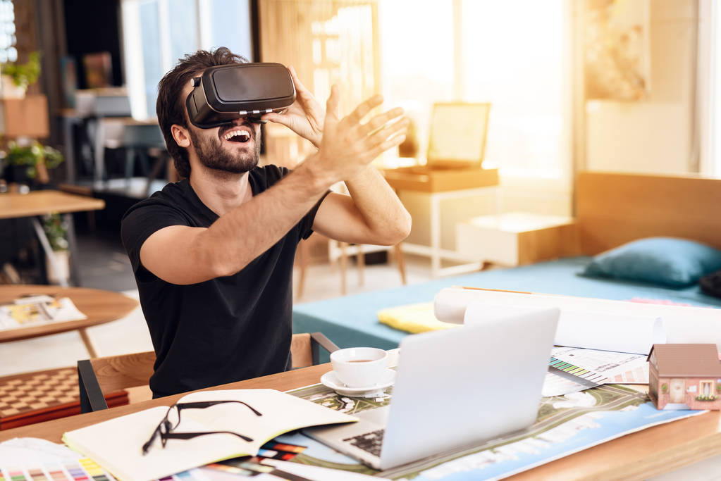Na volné noze vousatý muž pomocí virtuální reality v notebooku sedí u stolu. - Fotografie, Obrázek