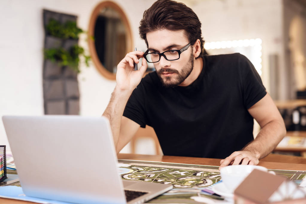 Freelancer barbu homme en t-shirt regardant ordinateur portable assis au bureau
. - Photo, image