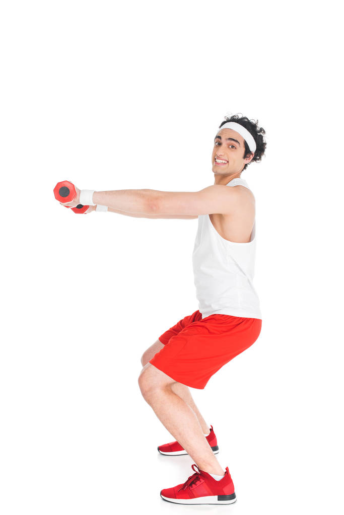 Zijaanzicht van lachende dunne sportman met halters geïsoleerd op wit - Foto, afbeelding