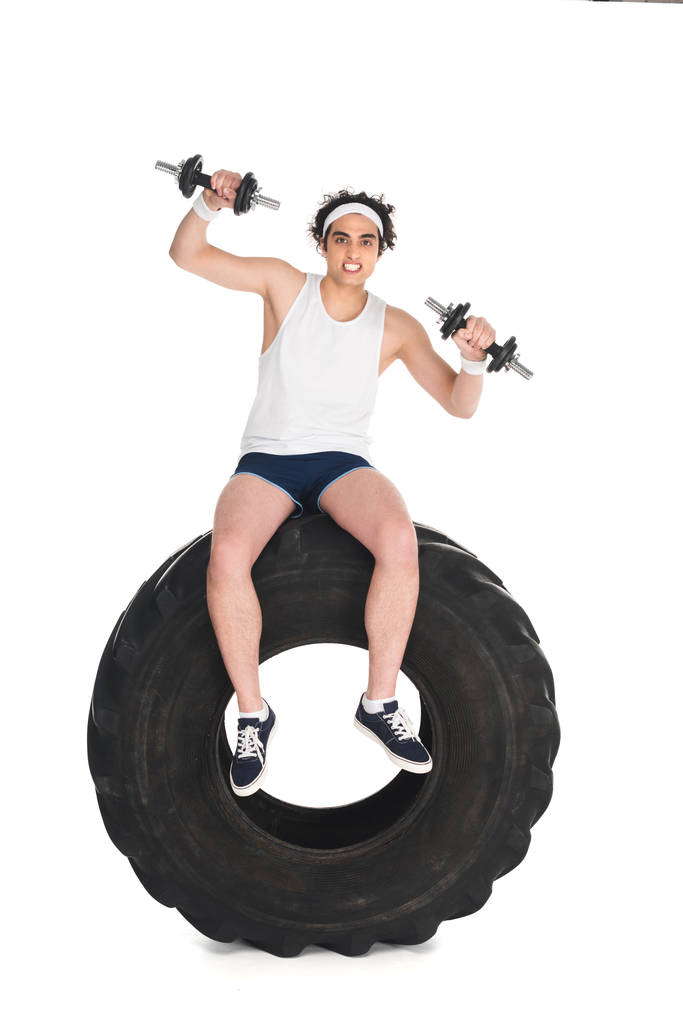Joven deportista delgado con mancuernas sentado en el neumático de la rueda aislado en blanco
 - Foto, imagen