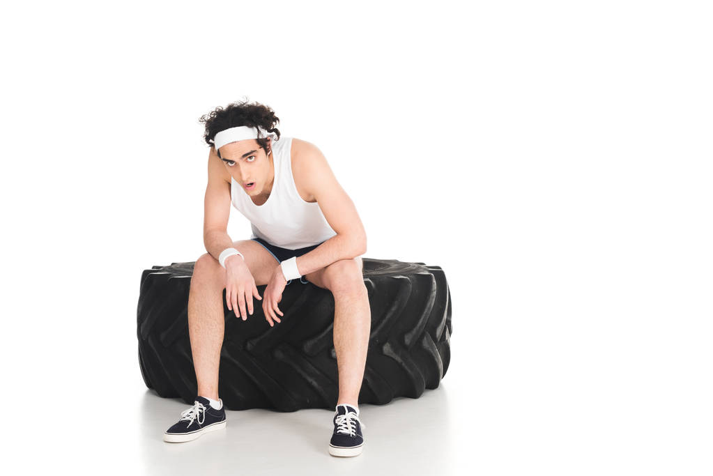 Lastik tekerleğin üzerinde beyaz izole oturan yorgun ince sporstman - Fotoğraf, Görsel