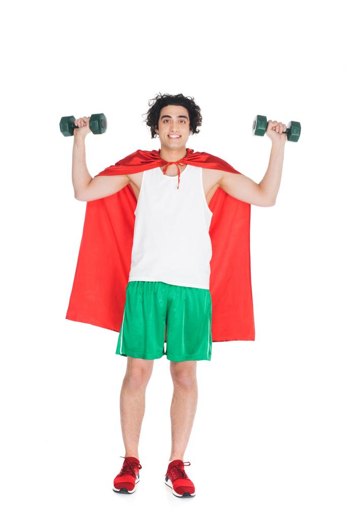 Lachende mager sportman met halters permanent in rode cape geïsoleerd op wit - Foto, afbeelding