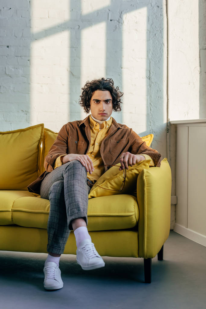 Nuori tyylikäs mies silmälasit kädessä istuu sohvalla
 - Valokuva, kuva