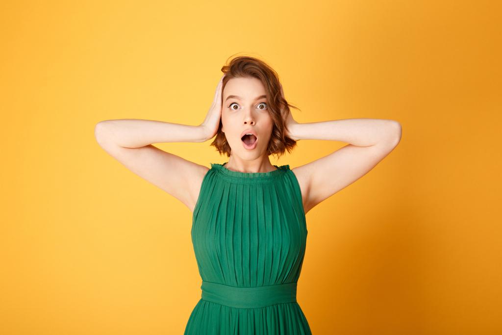 Portret van geschokt jongedame voor oren met handen geïsoleerd op oranje - Foto, afbeelding