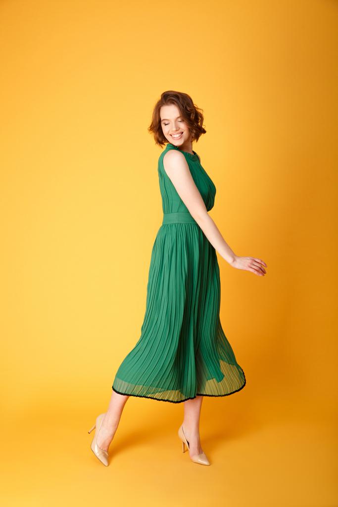 молода весела жінка в зеленій сукні ізольована на помаранчевому
 - Фото, зображення
