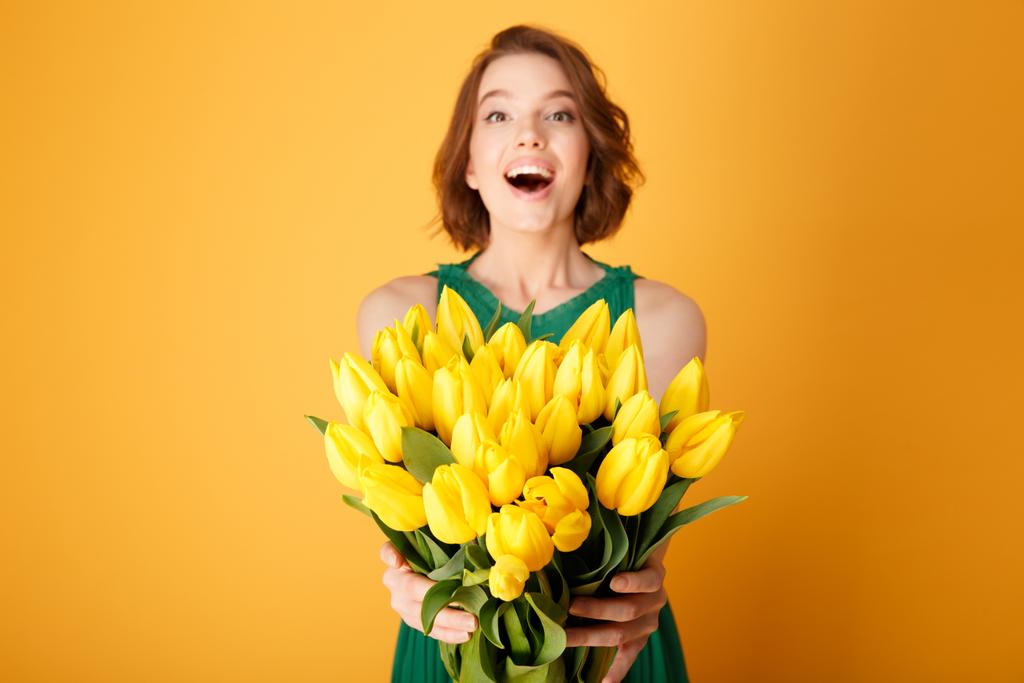 foco seletivo de mulher feliz apresentando buquê de tulipas de primavera amarelas em mãos isoladas em laranja
 - Foto, Imagem