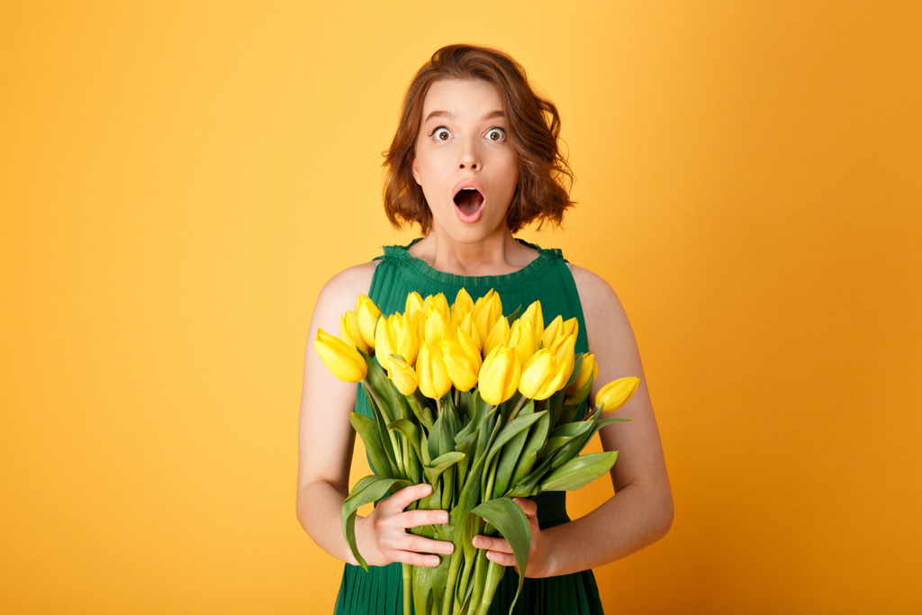 retrato de mujer conmocionada con ramo de tulipanes amarillos aislados en naranja
 - Foto, imagen