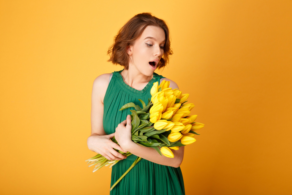 retrato de mulher surpreendida olhando para buquê de tulipas amarelas isoladas em laranja
 - Foto, Imagem