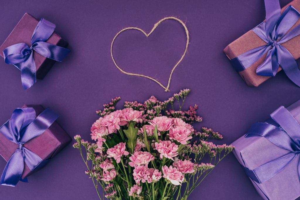 Strauß schöner rosa Blumen, herzförmiges Seil und Geschenkboxen auf violett - Foto, Bild