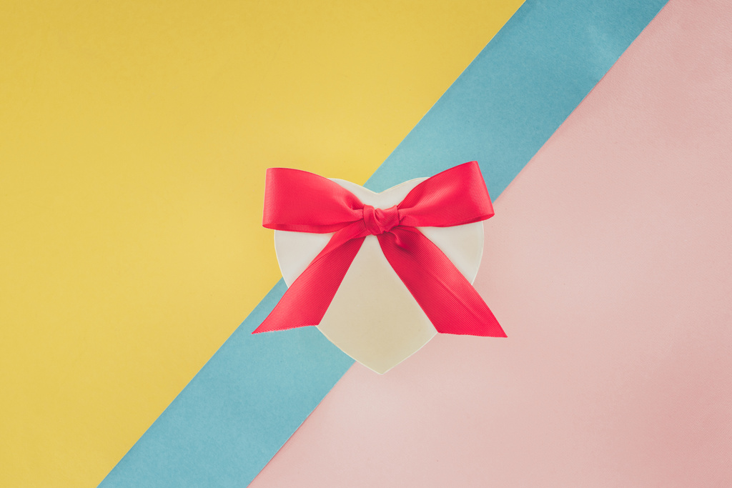 top view of white heart shaped gift with pink ribbon on colorful background - Photo, Image