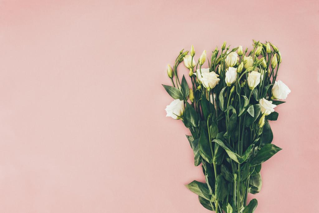 Strauß schöner weißer Eustoma-Blüten mit grünen Blättern auf rosa - Foto, Bild