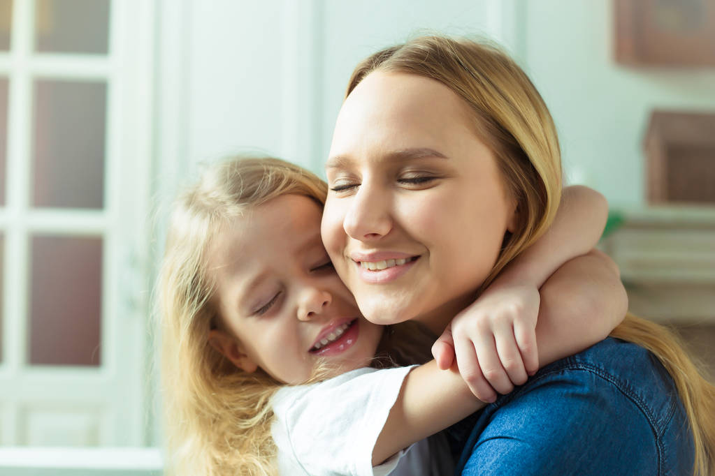 Amo-te, mãe! Mãe e filha se abraçam muito bem com os olhos fechados em casa no sofá
. - Foto, Imagem