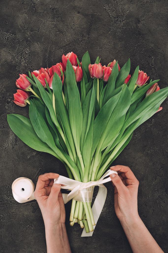 częściowy widok osoby dekorowanie bukiet pięknych tulipanów z wstążki - Zdjęcie, obraz