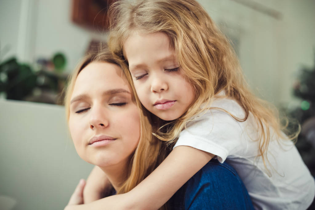 ¡Te quiero, mamá! Mamá y su hija se abrazan muy fuerte con los ojos cerrados en casa en el sofá
. - Foto, imagen