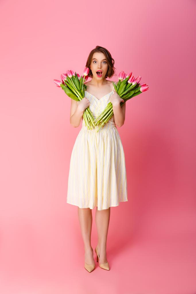 šokovaná mladá žena s kytice jarních květin izolované na růžové - Fotografie, Obrázek