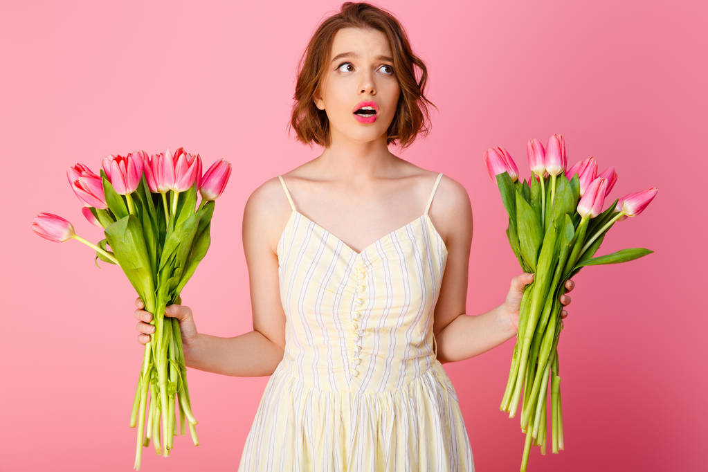 portrait of confused woman with bouquets of tulips isolated on pink - Photo, Image
