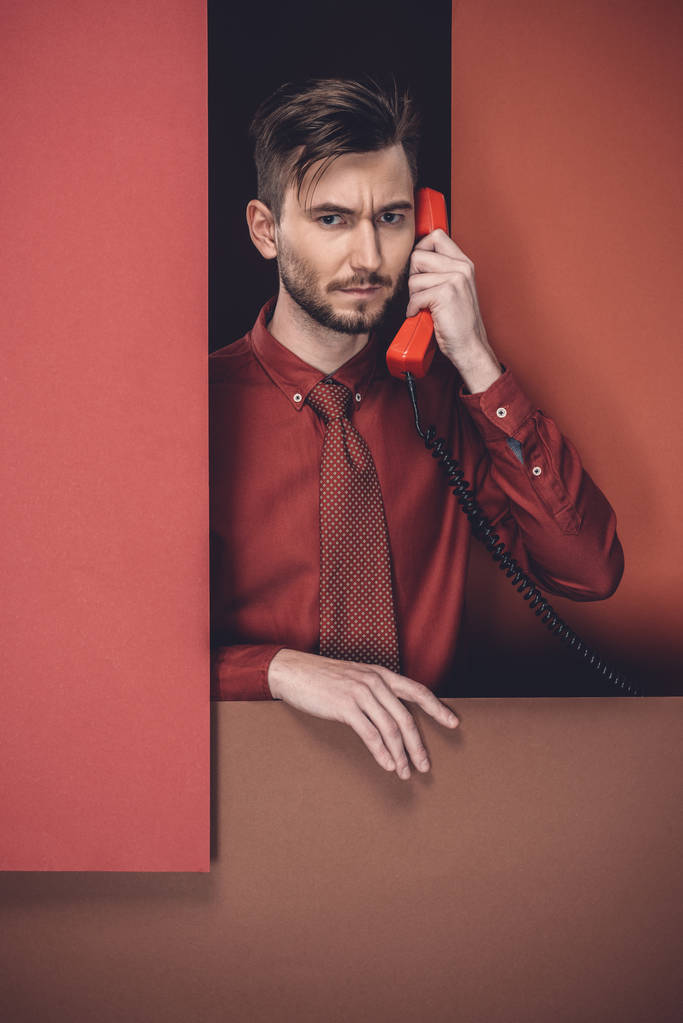 Thoughtful man holding phone headset by red paper walls isolated on black - Photo, Image