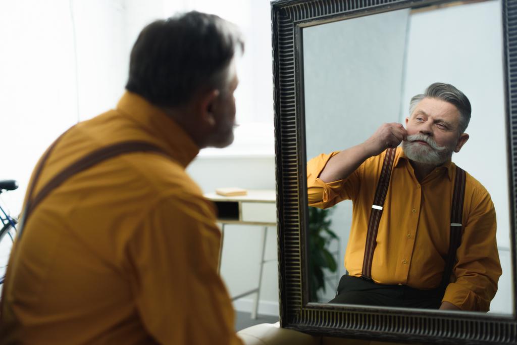 όμορφος γενειοφόρος άνδρας ανώτερος προσαρμογή μουστάκι και κοιτάζοντας καθρέφτη - Φωτογραφία, εικόνα