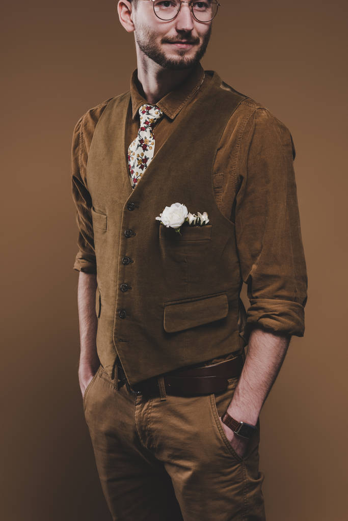 Молодой человек в винтажной одежде с бутоньеркой, изолированной на коричневом
 - Фото, изображение